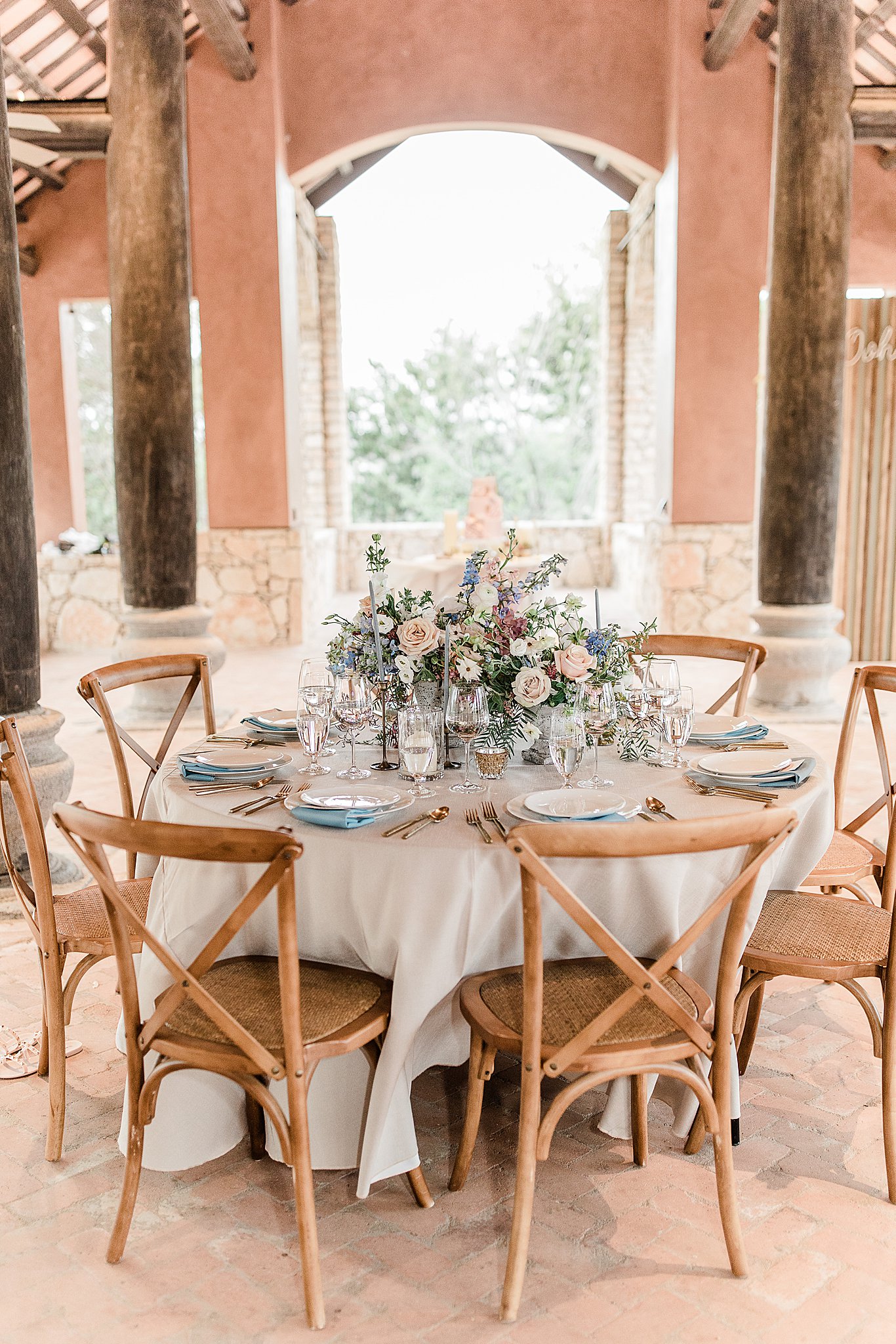 Romantic outdoor reception in Austin, Texas with blush, blue and cream florals, cream table linens, wooden chairs wedding reception