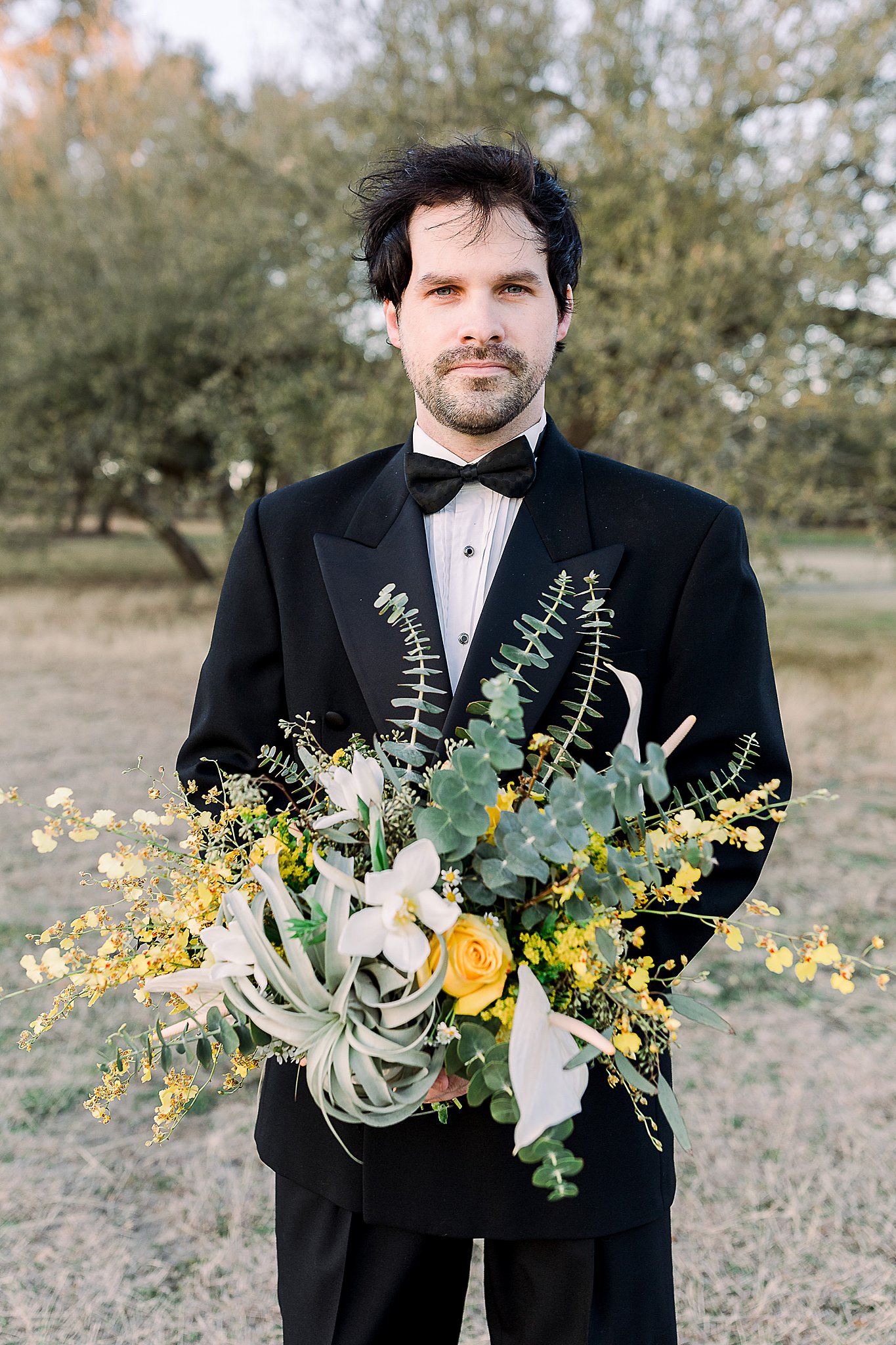 Groom posing with incredible floral installation with eucalyptus, succulents, and yellow flowers
