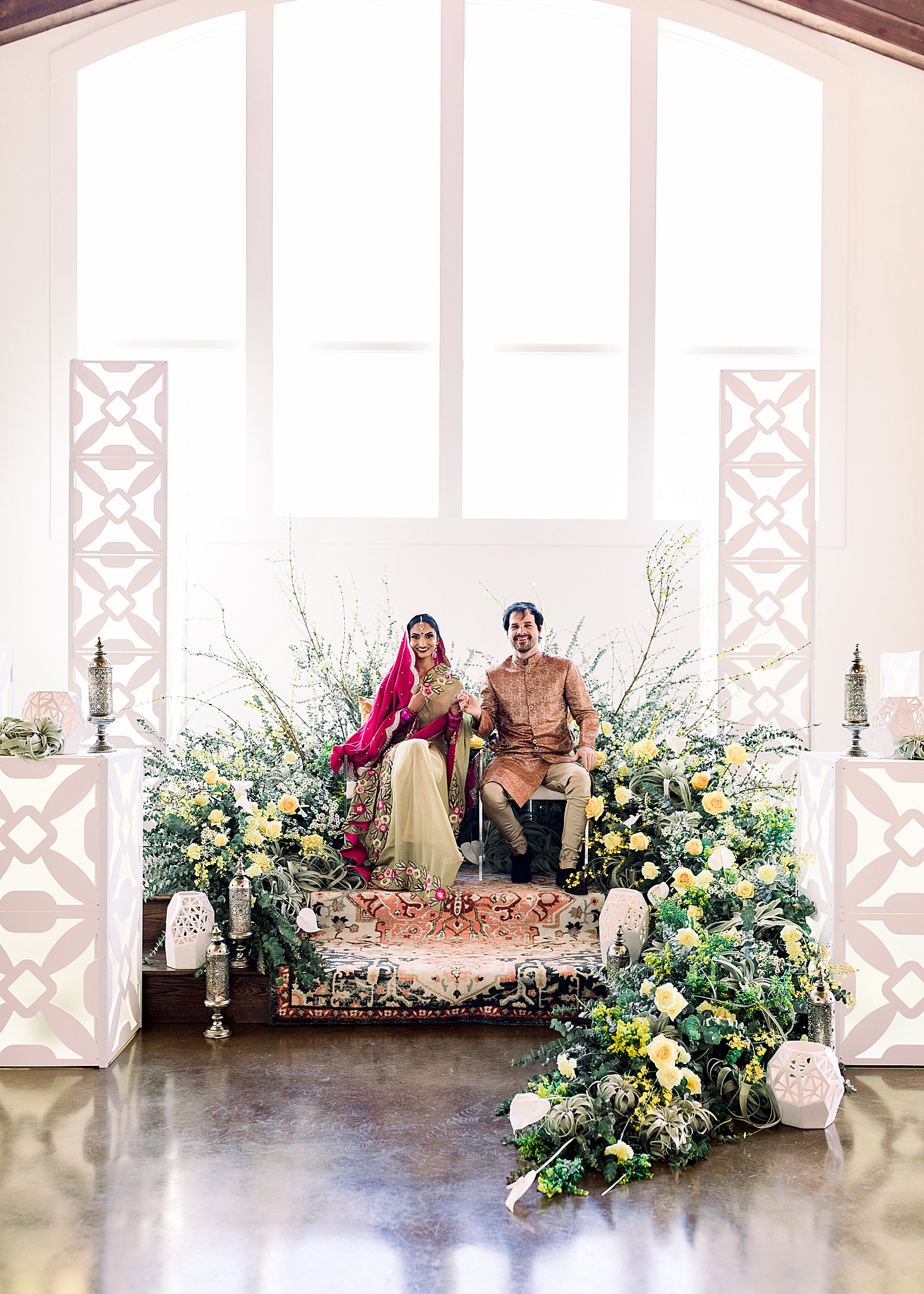 Sitting bride and groom on stage with yellow and green wedding florals in Sherwani and lehenga